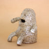 Side view and closeup photo of the Plonk handmade stoneware figurine. Sitting down, with two forward facing short legs, and two arms with holes. Figurine has a large mouth opening, and two small eye openings. 