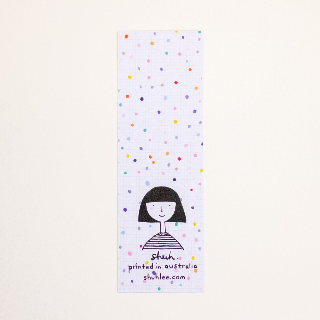 A tall, narrow bookmark featuring a white grid background with scattered multicoloured confetti dots and a simple black line drawing of a person near the bottom. Text on the card reads 'shuh.', 'printed in australia', and 'shuhlee.com'.