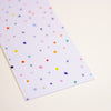 A rectangular sheet of white graph paper with a colourful polka dot pattern, photographed on a light cream background.