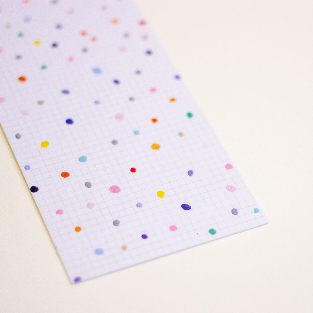 A rectangular sheet of white graph paper with a colourful polka dot pattern, photographed on a light cream background.