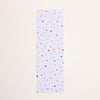 A postcard with a white grid background and scattered multicolour polka dots, displayed vertically against a solid off-white background.