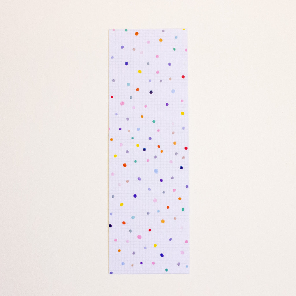 A postcard with a white grid background and scattered multicolour polka dots, displayed vertically against a solid off-white background.