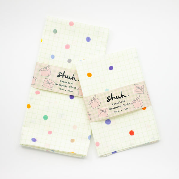 A Top view of the pop pop fuoshiki gift wrapping in retail packaging. Print is bright polka dots on a light grid background. 