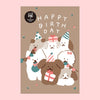 A birthday postcard featuring a illustration of several dogs wearing party hats and holding wrapped presents, with the words “HAPPY BIRTHDAY” in white at the top. The card has a warm taupe background and is centered on a light pink backdrop.
