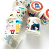 Several rolls of decorative washi tape with colorful illustrated patterns are arranged on a white background. The designs include vintage postmarks, stamps, a red telephone, a dog paw print, and cartoon characters.
