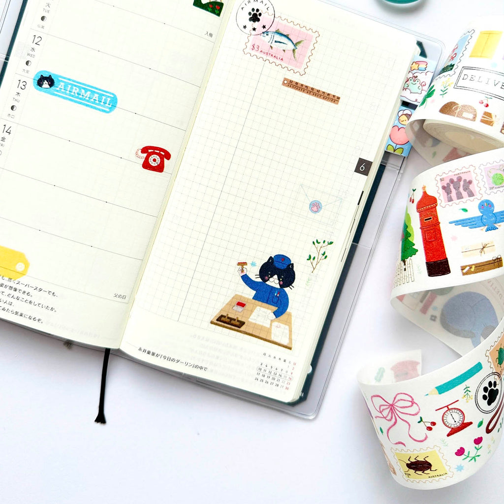 An open planner or journal with decorative stickers and a weekly layout, shown alongside rolls of colourful washi tape on a white surface.