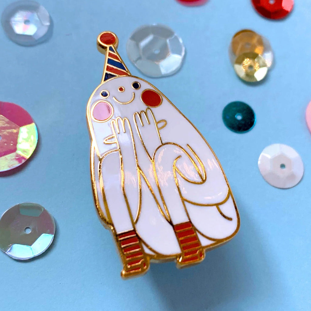 Decorative pin of a cartoon in a party hat on a blue background with colouful sequins.