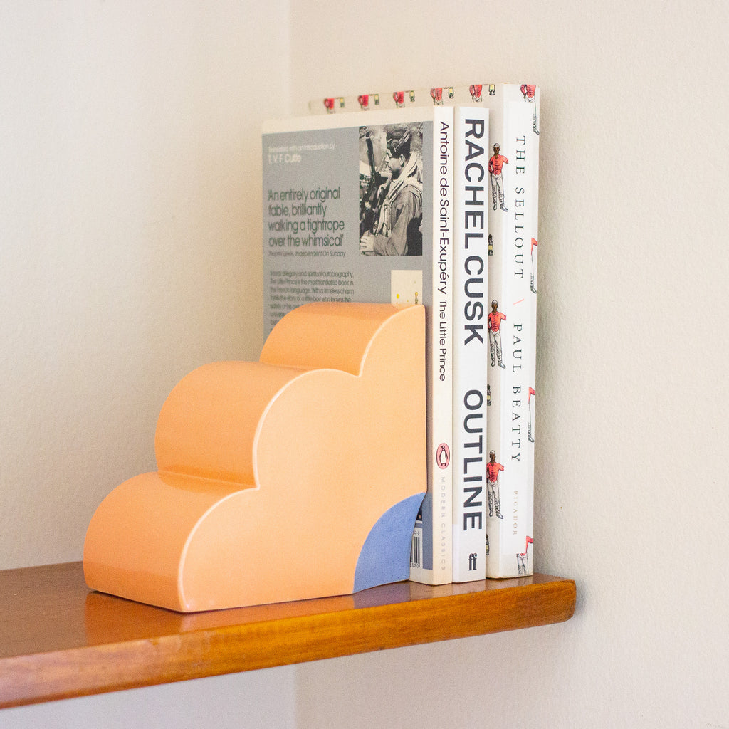 Peach bookend on a shelf, holding up 3 books. 