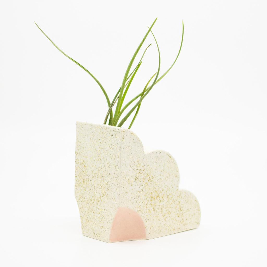 Ceramic bookend in a quarter flower shape. Speckled finish with pink highlight. Opening at top so bookend also functions as a vase. Front view. 