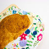 A close-up of a decorative clutch or pouch featuring a large brown rabbit illustration on a white background with a colourful floral print.