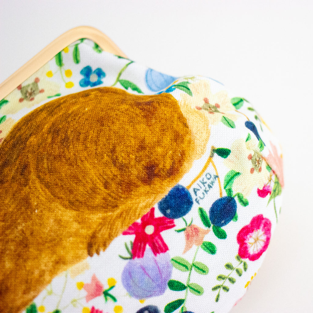 A close-up of a decorative clutch or pouch featuring a large brown rabbit illustration on a white background with a colourful floral print.