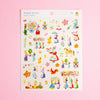 A sheet of colourful illustrated stickers titled 'Rabbit garden' by artist Aiko Fukuwa, featuring whimsical characters, flowers, and garden elements on a white backing card, set against a solid pink background.