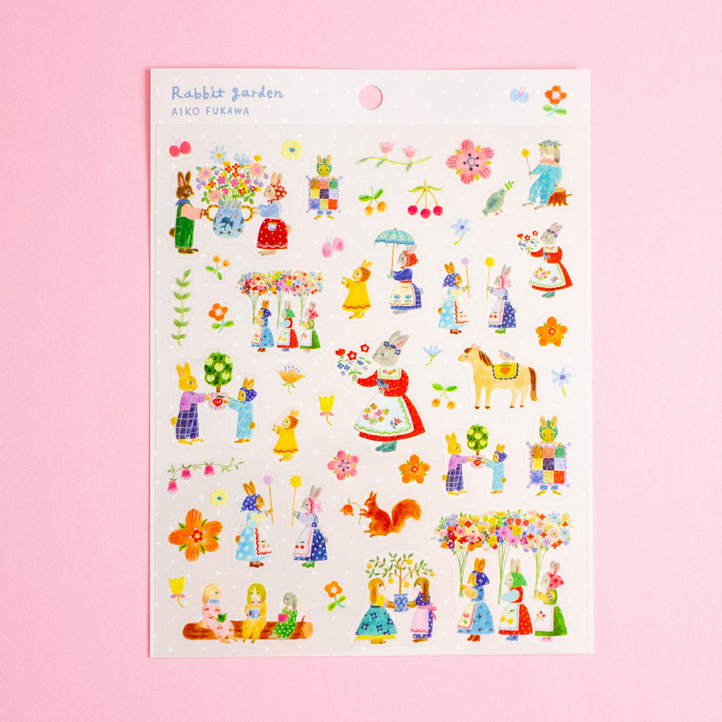 A sheet of colourful illustrated stickers titled 'Rabbit garden' by artist Aiko Fukuwa, featuring whimsical characters, flowers, and garden elements on a white backing card, set against a solid pink background.