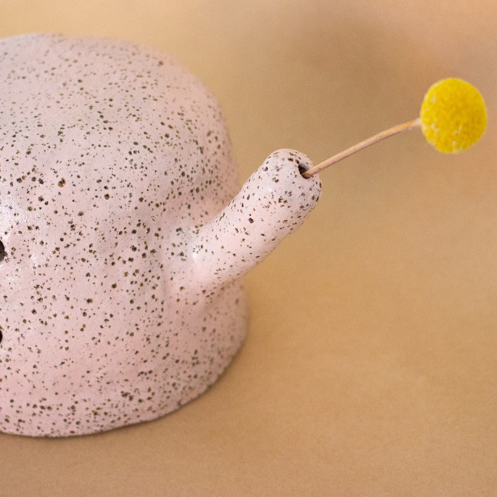 Closeup of the Rah figurine arm, which has a hole where you can place a flower. There is a stem and flower in the hole. 