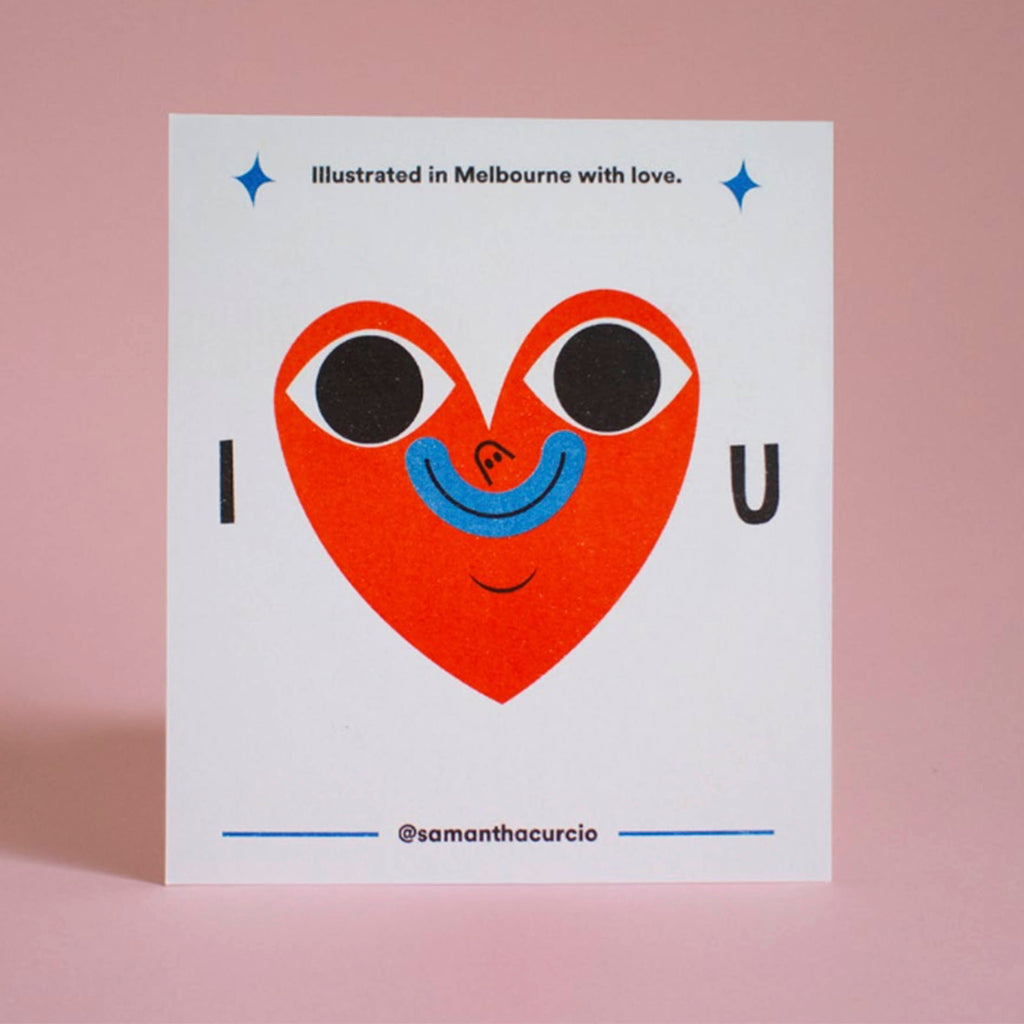 A square white art print or card featuring a stylized red heart with black eyes and a blue smile, with the text 'Illustrated in Melbourne with love.' and '@samanthacurcio' on a soft pink background.