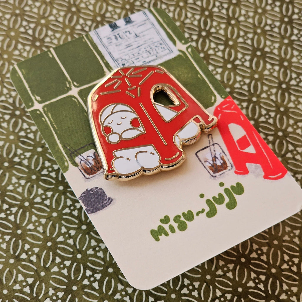 A Misu Juju enamel pin shaped like a red plastic stool with a cute cartoon character inside, mounted on its illustrated backing card.
