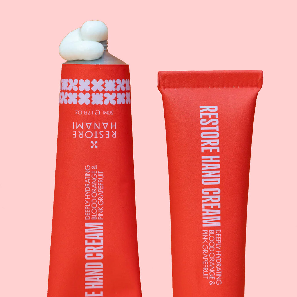 Two red hand cream tubes with white text on a pink background