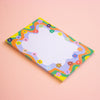 A rectangular notepad with a colourful retro wavy border and small flowers, featuring a white lined writing area, set against a solid light pink background.