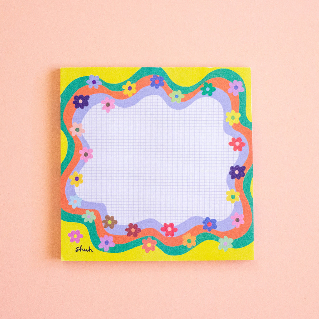 A square notepad with a colourful retro wavy border and small flowers, photographed flat against a soft peach background.