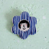 Flower-shaped brooch with a face design and striped petals. 