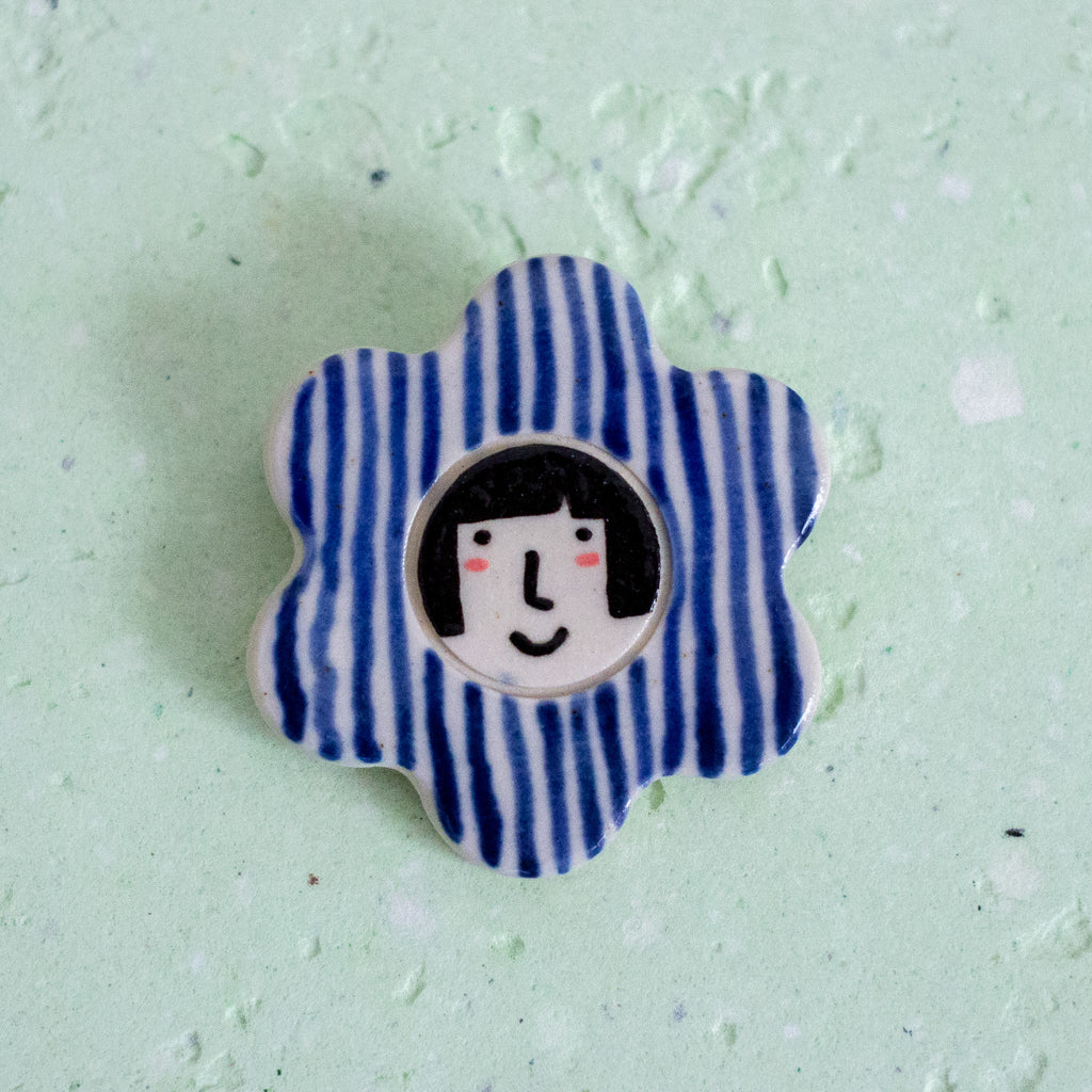 Flower-shaped brooch with a face design and striped petals. 