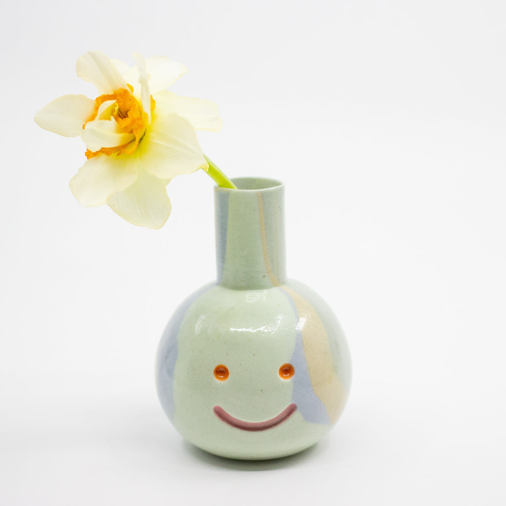 Smiley face vase with a yellow flower on a white background