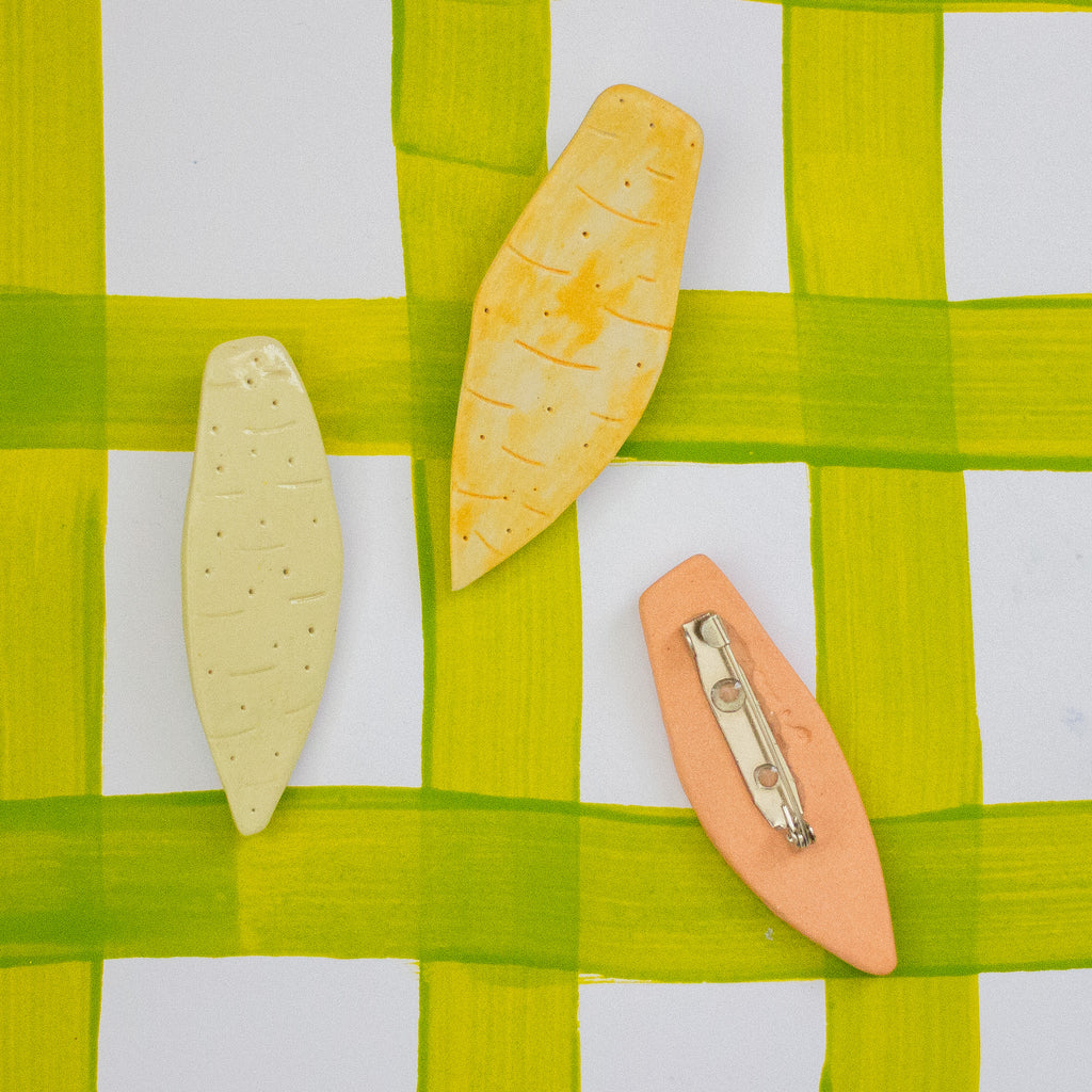Three ceramic vegetable-shaped brooches on a green and white checkered fabric background