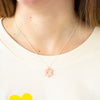 Necklace with a pink flower pendant worn by a person on a white background