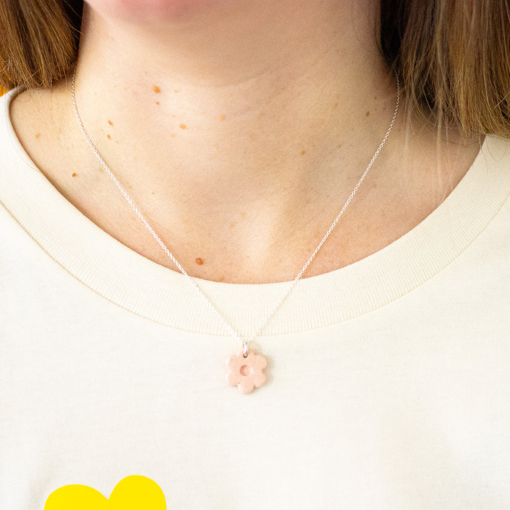 Necklace with a pink flower pendant worn by a person on a white background