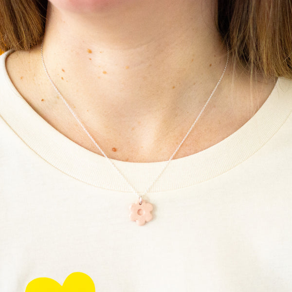 Necklace with a pink flower pendant worn by a person on a white background
