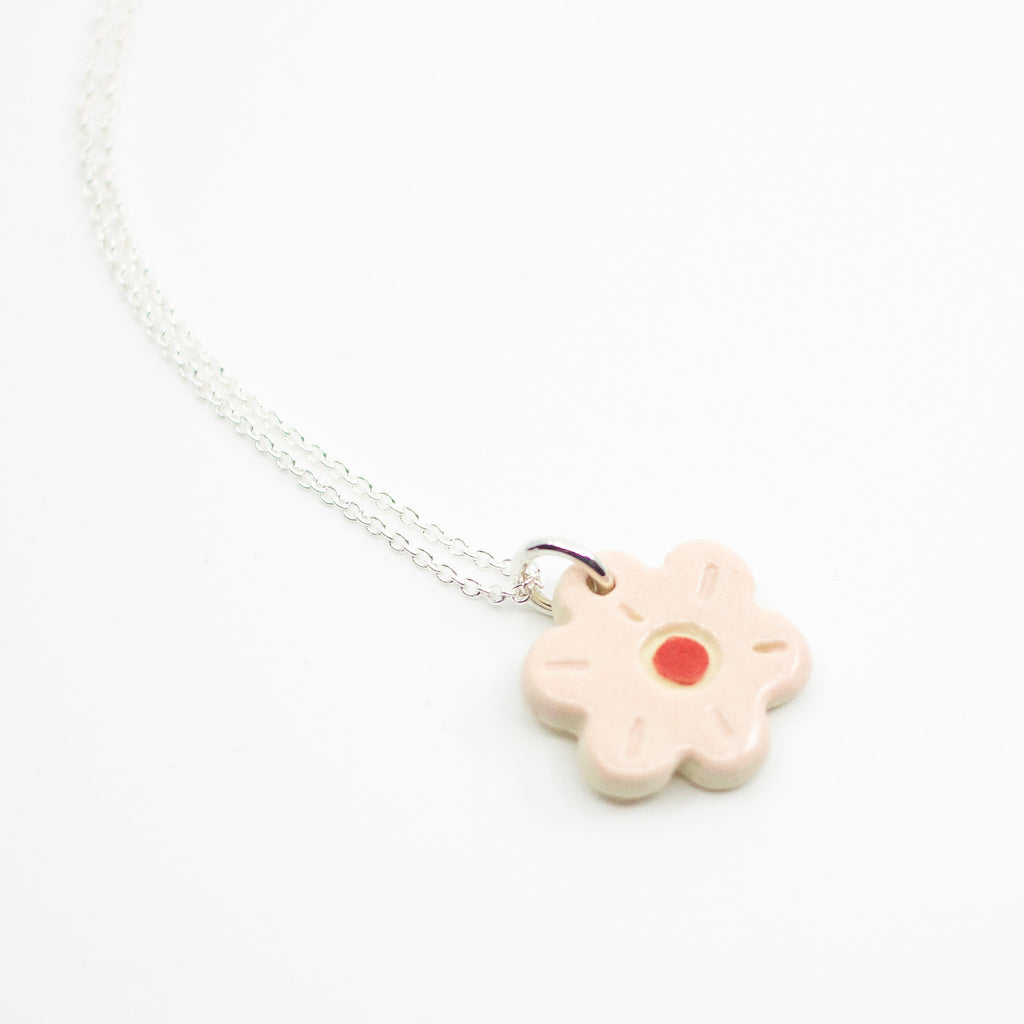 Sterling silver necklace featuring a light pink ceramic flower-shaped pendant with a red dot in the centre, displayed on a white background.