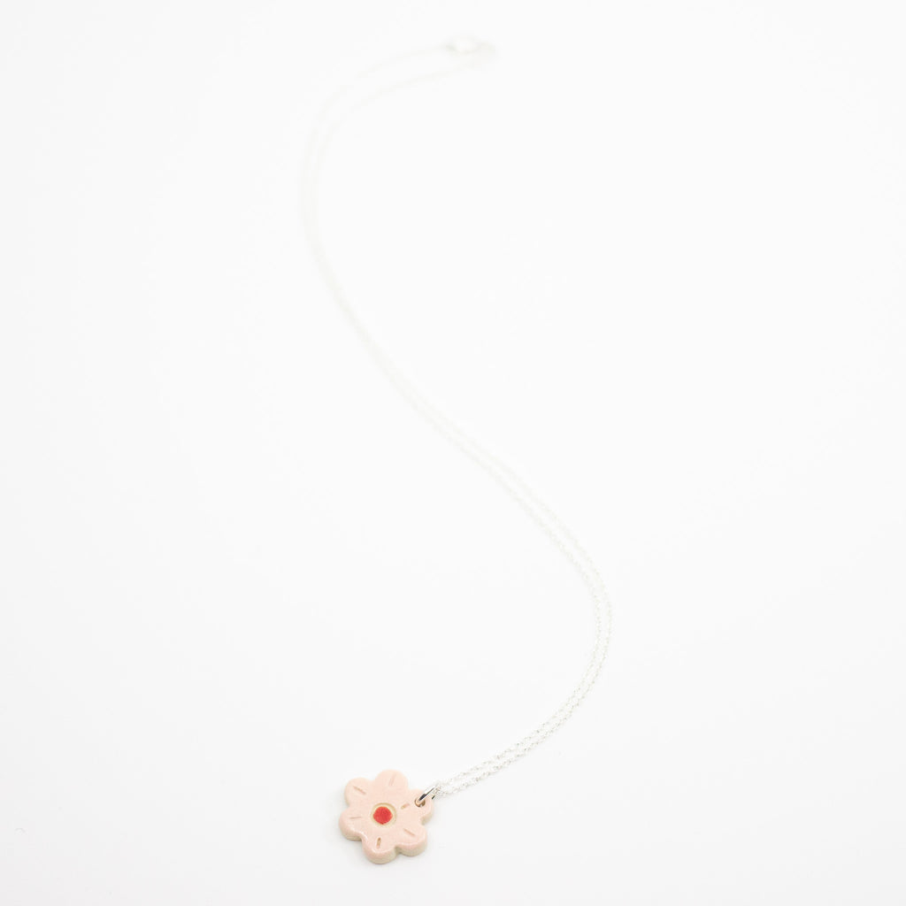 Sterling silver necklace featuring a light pink ceramic flower-shaped pendant with a red dot in the centre, displayed on a white background.