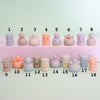 A set of pastel-coloured ceramic figurines and small cylinders with simple smiley faces, arranged in two rows on a pale mint background. Each piece is numbered from 1 to 18 with black text above and below.