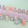 A collection of pastel-coloured, speckled ceramic figurines with simple painted faces, arranged on a light mint green surface and a white display riser.