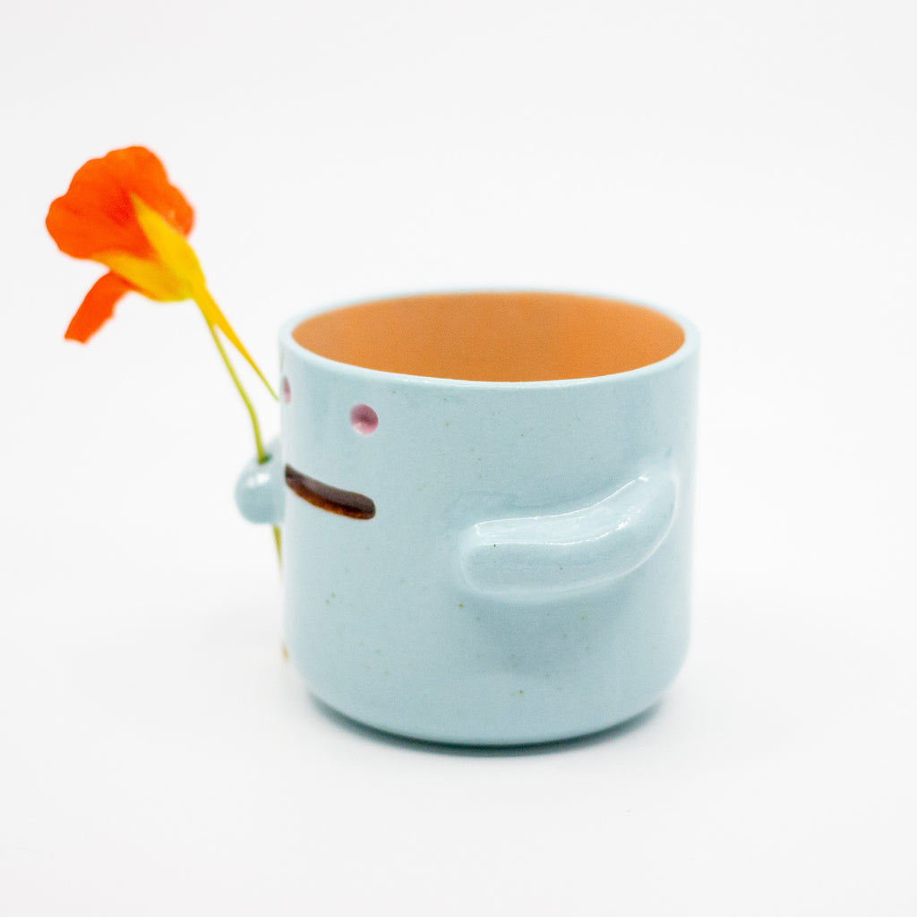 Light blue mug with a smiling face design and a red flower on a white background