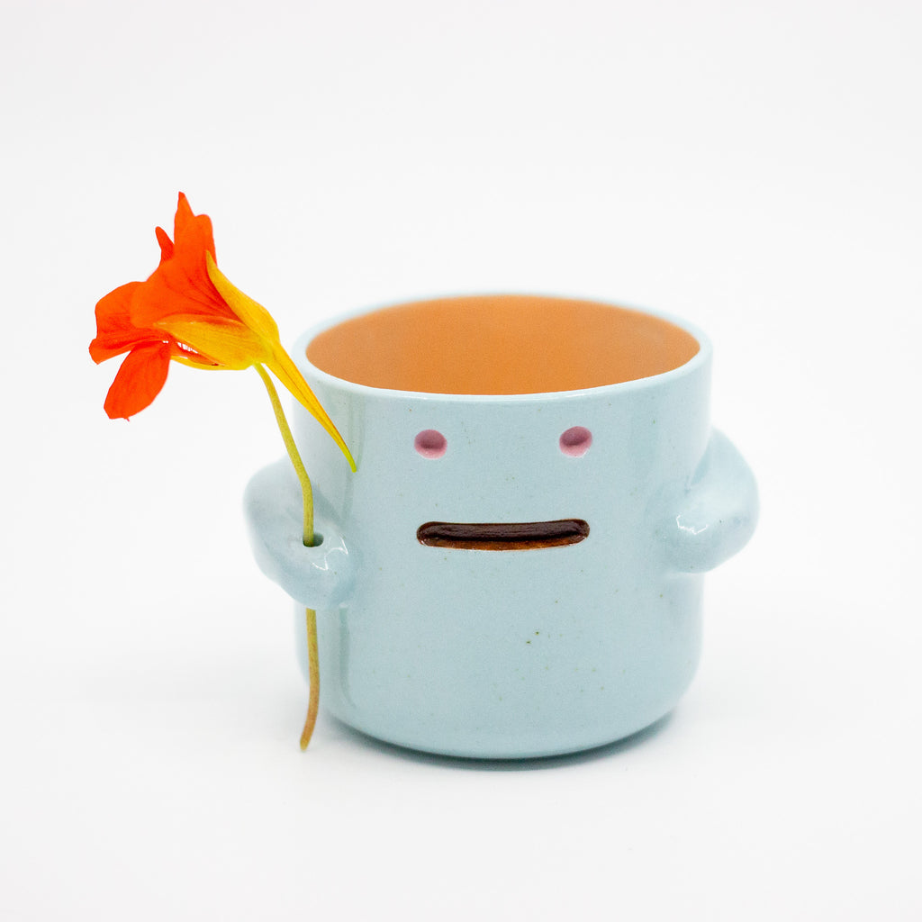 Ceramic mug with face holding a flower on a white background