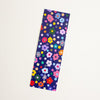 A rectangular bookmark, featuring a colourful floral and polka dot pattern on a dark navy background, shown on a plain off-white surface.