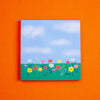 A square art print depicting a colourful flower meadow under a blue sky, displayed against a solid orange background.