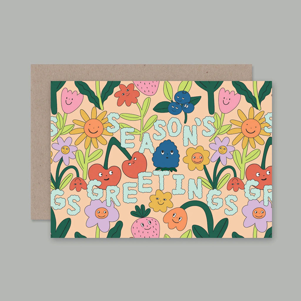 A greeting card with a colourful cartoon floral pattern and the words 'SEASON'S GREETINGS' across the front, shown with a plain kraft envelope behind it on a light grey background.