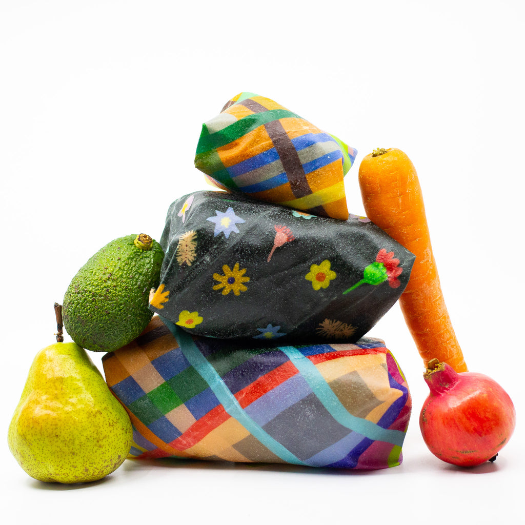 A Front view of the 3 bees wax food wraps. All are in use protecting food. There are fruits and vegetables around the wraps. 