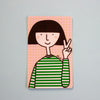 A rectangular art print or card featuring a minimalist cartoon illustration of a person with a black bob haircut, pink grid background, and green-and-white striped shirt, shown against a light blue background.