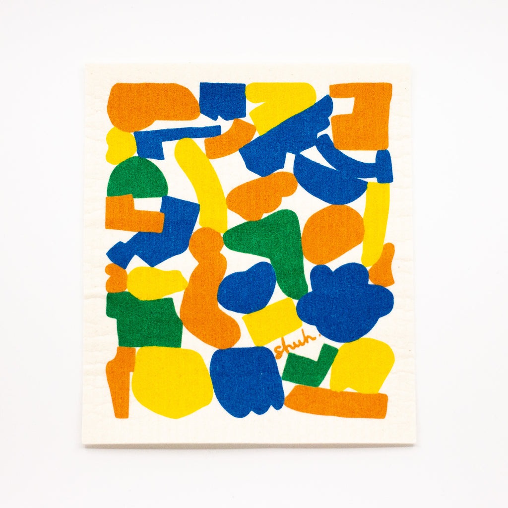 Top view of the shuh and spruce eco friendly dishcloth. Print features multicoloured shapes in green, orange, yellow, and blue. White background. 