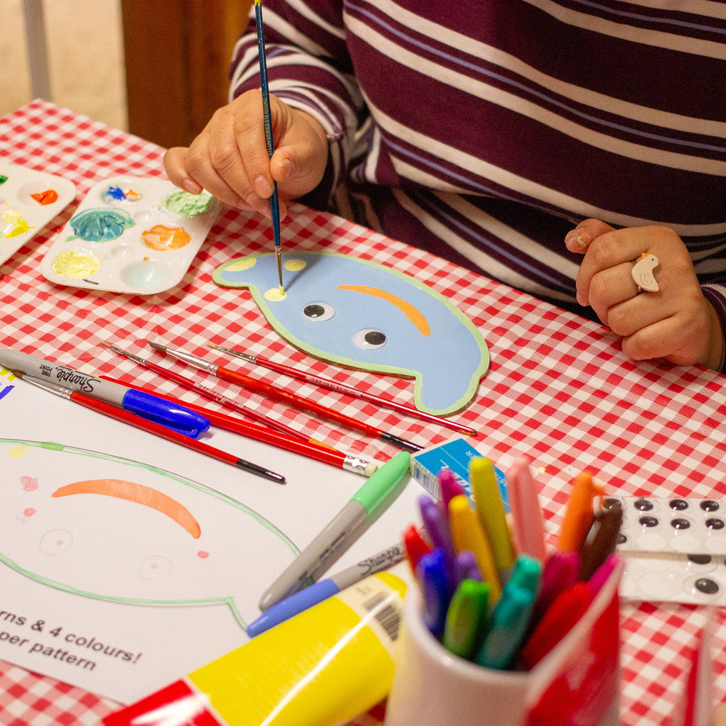 A person applying paint on a wooden template with art supply on a table