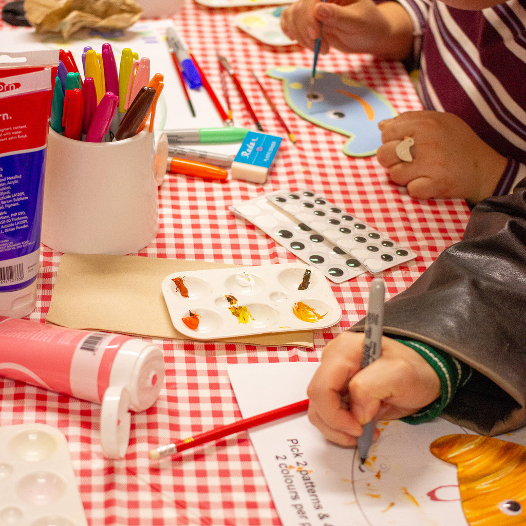 Two person applying paint on a wooden template with art supply on a table