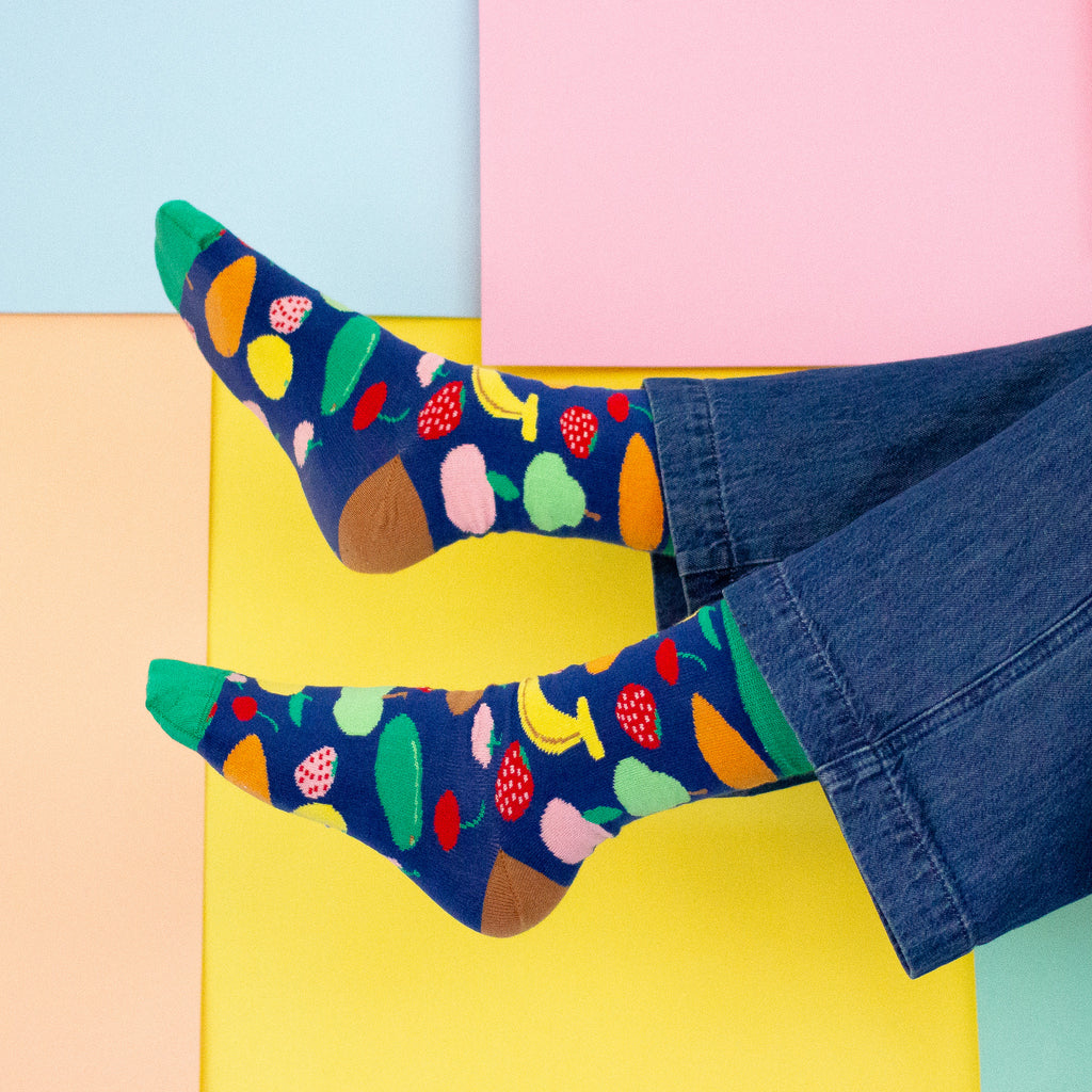 Colorful socks with fruit pattern worn by a person on a multicolored background