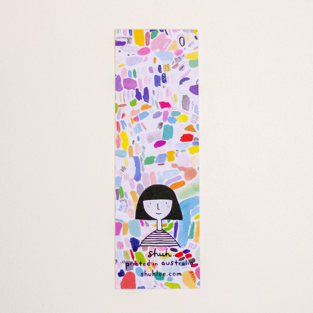 A tall, narrow printed  bookmark with a colourful abstract pattern and a simple black-haired girl illustration near the bottom. The text 'shuh. and 'printed in australia' with 'shuhlee.com'.