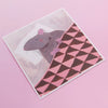 An illustrated square print of a rat sleeping on a pillow and tucked in under a blanket with white border photographed against a pink backdrop. 