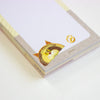 A close-up of a notepad with a white writing area, a gray textured border, and a peeking cat face illustration in the lower left corner. 