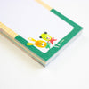 A close-up of a notepad with a green border and cartoon animal illustrations, photographed on a clean white background.