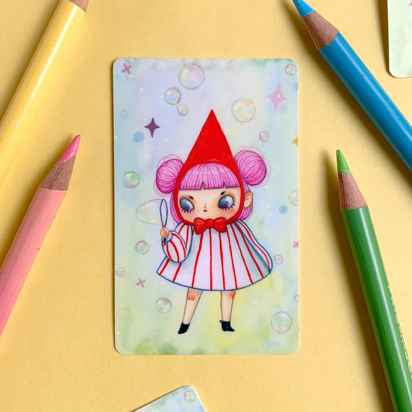 Colourful illustration of a character on a card with coloured pencils around it